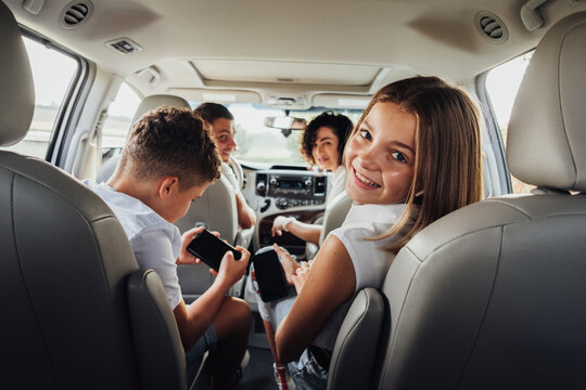 Cheerful Caucasian Teenage Girl Smiles Into the Camera While Sitting in Minivan Car with Her Brother, Mother and Father, Happy Four Members Family Enjoying Weekend Road Trip