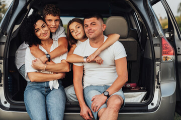Portrait of Happy Four Caucasian Members Family Sitting in Trunk of the Minivan Car, Mother and Father with Two Teenage Children, Son and Daughter Having Weekend Outdoors