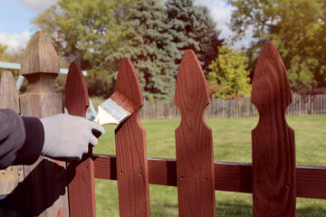 Man is painting wooden fence with brown paint outside