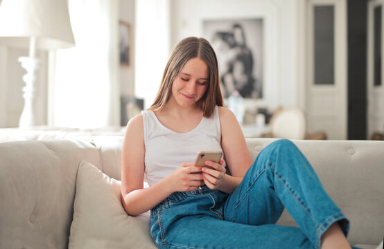 young woman uses a smartphone sitting on the sofa at home
