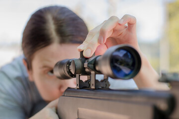 A female sniper adjusts an optical sight while looking into it