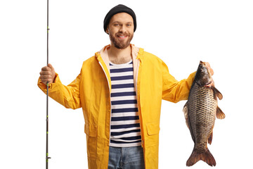 Happy young fisherman holding a carp fish and a fishing rod and smiling at camera