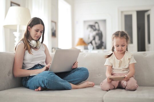 young woman and little girl use a computer and phone sitting on the sofa at home