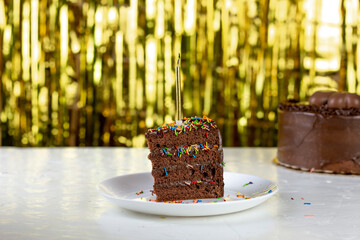 birthday party background. Chocolate cake and cake slice with gold candle, on shine bokeh gold background.