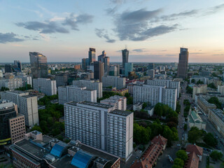 Centrum Warszawy, widok na bloki, wieżowce mieszkalne i biurowce, zbliżenie z lotu ptaka z drona, zachód słońca, wiosna, zielone drzewa, niebieskie niebo