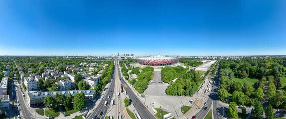 Zatłoczone rondo Waszyngtona w Warszawie w słoneczny dzień z lotu ptaka z drona, w tle stadion narodowy, dużo zieleni, wiosna - obrazy, fototapety, plakaty
