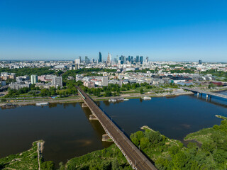 Widok na cenrum Warszawy z lotu ptaka z drona, widoczny most kolejowy oraz most Świętokrzyski, wiosna, dużo zieleni i niebieskie niebo