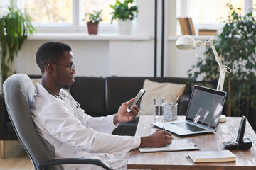 Medium side view portrait of modern young adult Black doctor wearing white coat and eyeglasses