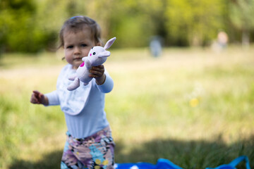 baby girl holds rabbit toy, toddler having fun at summer outdoor - obrazy, fototapety, plakaty