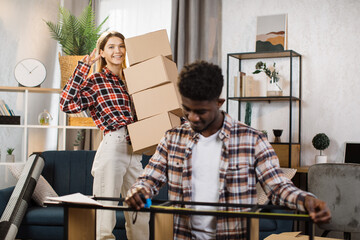 Cute caucasian woman making peace sign joyfully to camera while holding cardboard boxes at room....