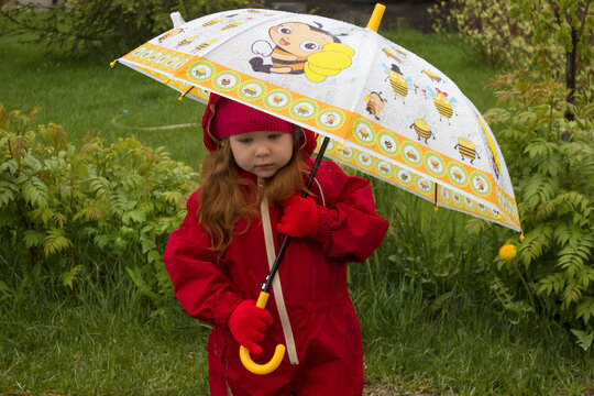 a little girl in the spring in the rain. a girl in a red raincoat and with a yellow umbrella