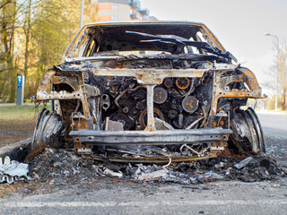 Close low angle front view to the burned car on the street during the day. Selective focus on burned engine.