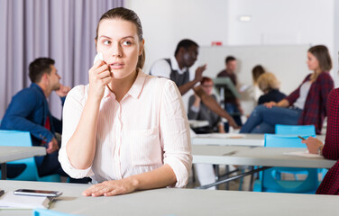 Portrait of frustrated young woman student sitting separately in classroom in break between lessons