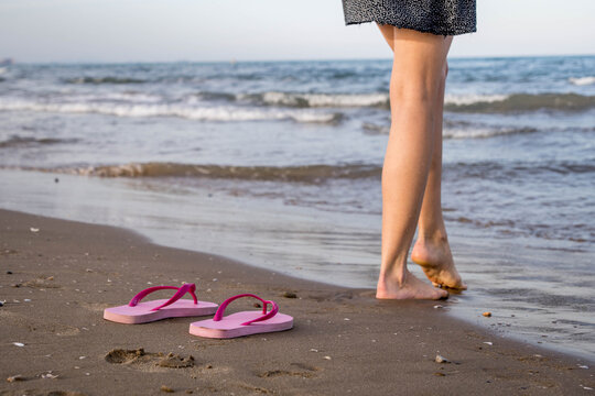Pretty View of a Pink Flip Flops Sandals Next to a Woman's Bare Feet on the Beach Shore with Wet Sand