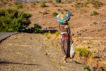 Woman walks with basket to carry injera in Ethiopia - obrazy, fototapety, plakaty