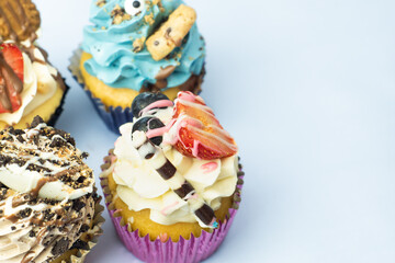 Colorful, funny and delicious muffin cupcakes collection decorated in various styles. Pastries with cream, fruits, cookies and chocolate on light blue background.