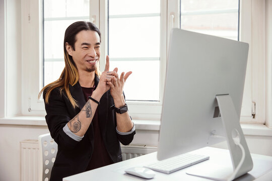 Mid adult man using sign language in front of computer