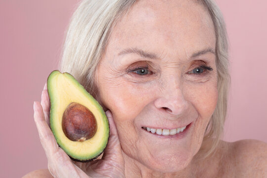 Studio shot of smiling senior woman holding halved avocado