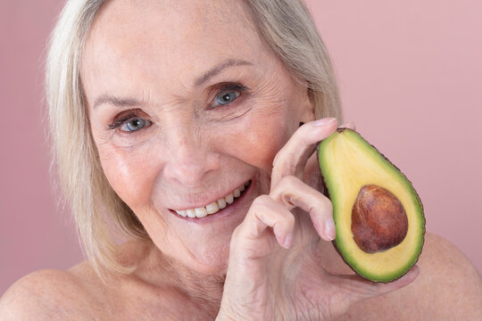 Studio portrait of smiling senior woman holding halved avocado