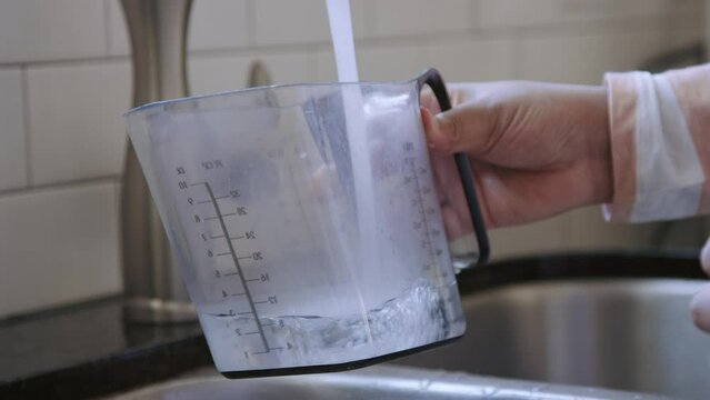 Close on pitcher being filled with tap water to 12 oz in kitchen sink