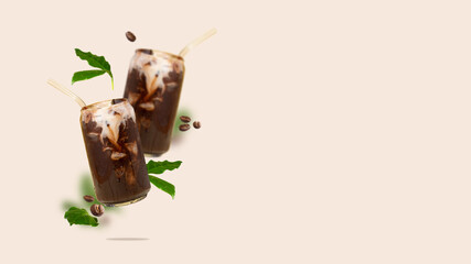 Two can-shaped glass with iced coffee, coffee beans and leaves in the air. Flying Cold coffee with non-dairy milk. Modern and creative composition of flying summer vegeterian drink copy space