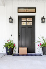 A blank cardboard box package delivered to the front door of a modern farmhouse style home. A...