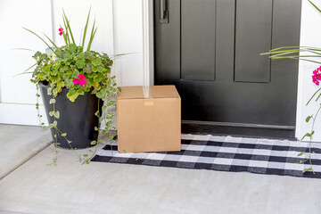 A blank cardboard box package delivered to the front door of a modern farmhouse style home. A...
