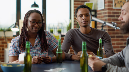 Portrait of african american man playing board games with cards and serving alcoholic beer in...