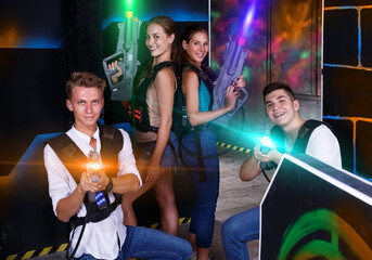 .Group portrait of cheerful girls and guys with pistols in their hands in dark laser tag room