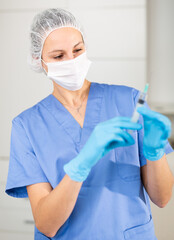 Nurse in a protective mask, working in the hospital, stands with a syringe filled with medicine in the treatment room