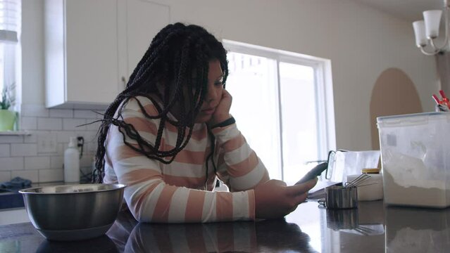 Black teenage girl scrolls through social media feed, bored in kitchen