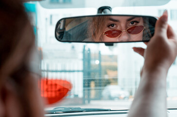 Non-binary young driving a car looking in the rear view mirror