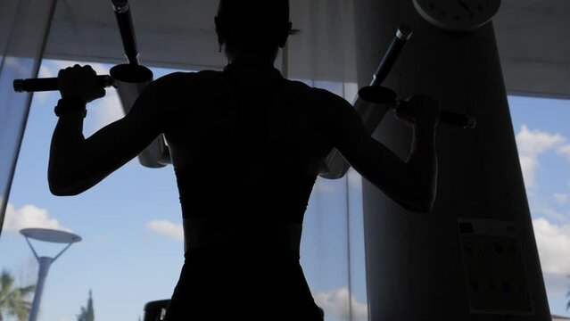 Silhouette of  muscular woman doing pull-ups at gym.