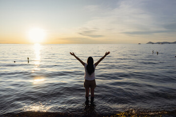 silhouette of a woman raising her arms in front of the sunset on the lake