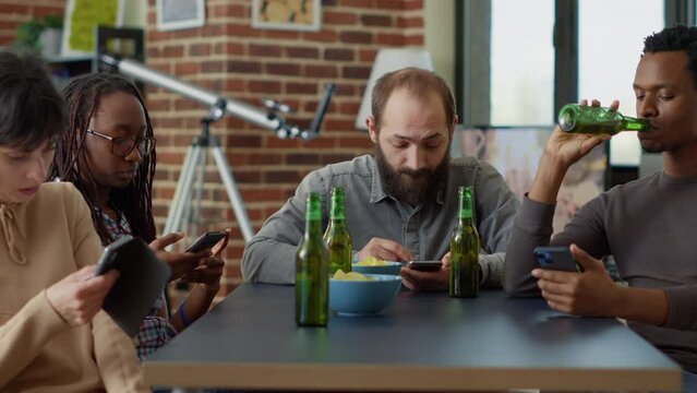 Millennial people scrolling through internet on smartphone instead of talking to each other at home gathering. Group of friends browsing social media website on mobile phone network.