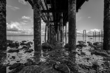 Barnacle covered pillars hold up a wooden fishing pier over Puget Sound on a cloudy late morning.