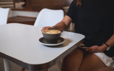Closeup image of a woman holding and drinking coffee in cafe