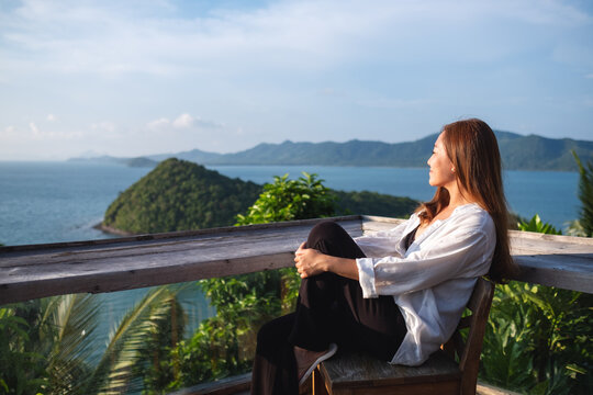 Portrait image of a young asian woman sitting and looking at a beautiful sea view from resort terrace