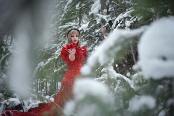 Young woman in the red dress walks in the winter forest.