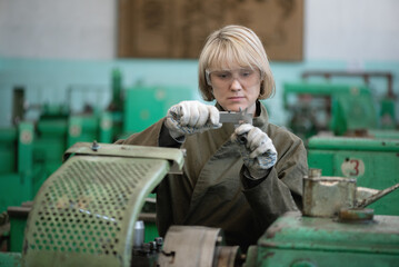 Woman worker with calipers in the hands near the lathe machine concept.
