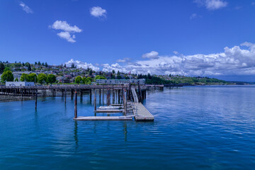 An empty boat tied to a wooden dock floats on the Puget Sound under a cloudy blue sky at Commencement Bay in Tacoma, Washington.