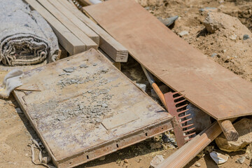 Rusted garden rake under piece of flat-board at construction site.
