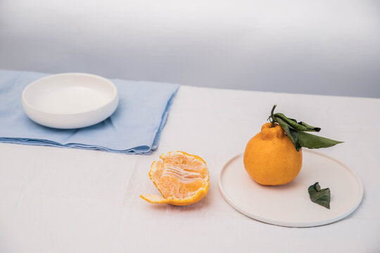 still life with fruit on the dining table. mineola on a white dining table. mineola with leaves and scrapings. still life with orange citrus fruits