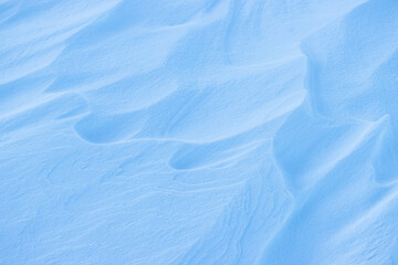 Fototapeta na wymiar Snow texture. Wind sculpted patterns on snow surface. Wind in the tundra and in the mountains on the surface of the snow sculpts patterns and ridges (sastrugi). Arctic, Polar region. Winter background