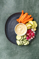 Fototapeta na wymiar Healthy snack chickpea hummus with various fresh vegetables and cereals on a gray platter. Cucumbers, radishes, celery, carrots, tomatoes, zucchini, red onions, parsley, cilantro. Healthy food