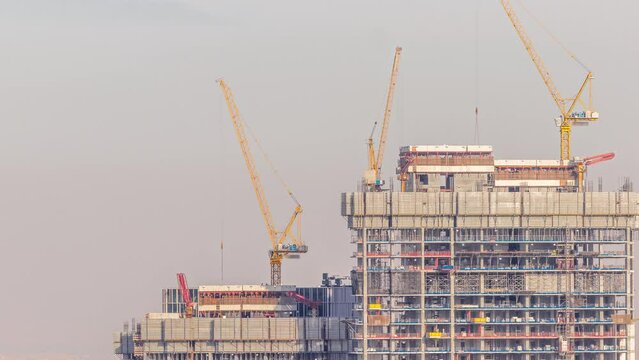High buildings under construction and many yellow cranes in downtown timelapse at evening during sunset. Active work at construction site of new towers and skyscrapers.