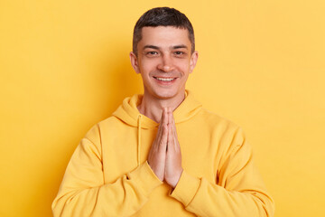 Indoor shot of positive man wearing casual style hoodie, posing isolated over yellow background,...
