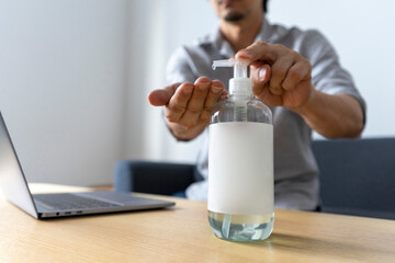 Hand sanitizer gel standing on wooden table. Adult Asian man cleaning hand with sanitizer gel while using laptop computer.