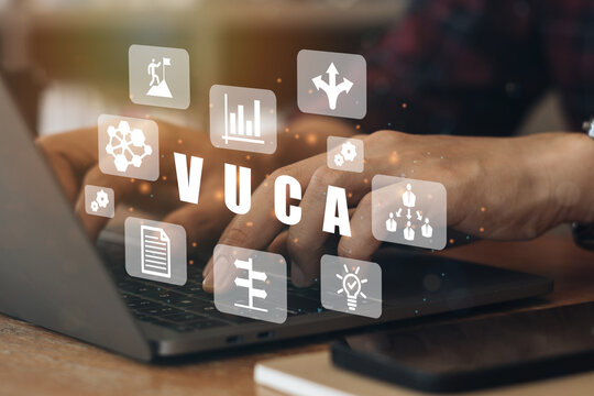 Businessmen using a computer to VUCA text surrounded by volatility, uncertainty, complexity, ambiguity icons. Background, copy space.