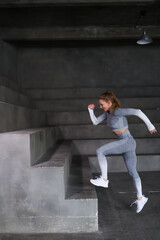 Beautiful strong muscular woman practicing sports in gym. Healthy woman trainer in grey sportswear training alone. Fit girl doing press indoors, training hard with barbells and dumbbels. Stretch, jump